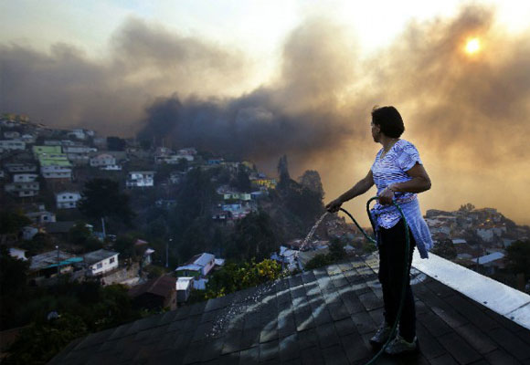 Una mujer humedece el tejado de su casa por temor a que prenda fuego en el cerro Ramaditas por un fuego activo, en la ciudad de Valparaíso, el 13 de abril de 2014. EFE/Felipe Trueba